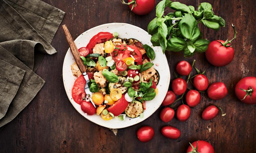 An plate of panzanella salad with basil and tomatoes on the side