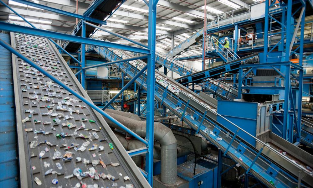 Wide angle view of a conveyor belt in a plastics recycling facility carrying plastic waste to be recycled