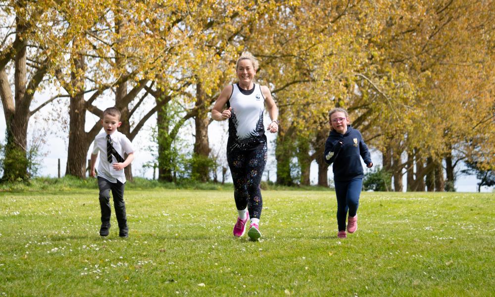 A group of school children and their teacher, running, in their school field. 