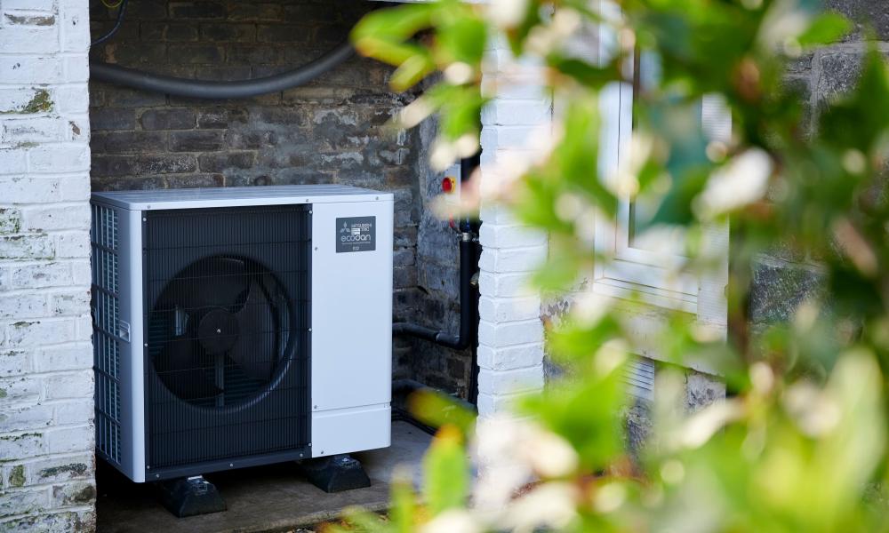 A heat pump on the side of an Edinburgh home. Green foliage in the forefront.