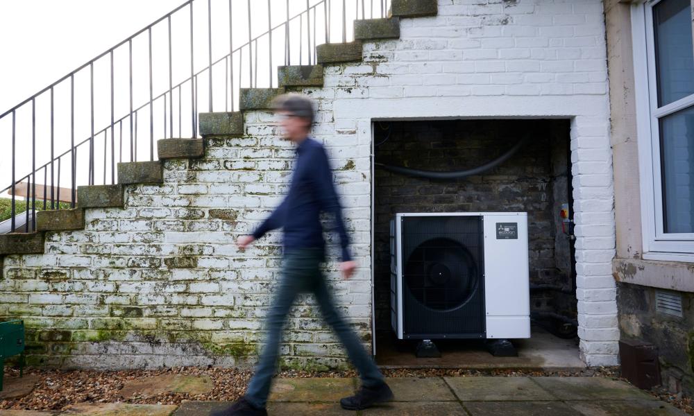 Huw walking past his heat pump outside their Edinburgh home. They're both smiling at the camera.
