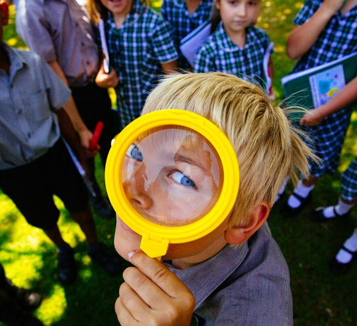 A boy looks through a magnifying glass. Him and his schoolmates have been working with WWF to learn more about nature in their school