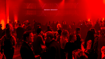 A large room with red stage lighting with people gathered around talking