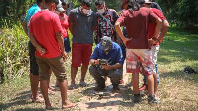 A group of nine Indigenous People watching a demonstration of how to use a drone