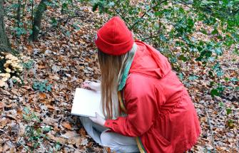 Artist Harriet Gardiner crouching in forest drawing funghi