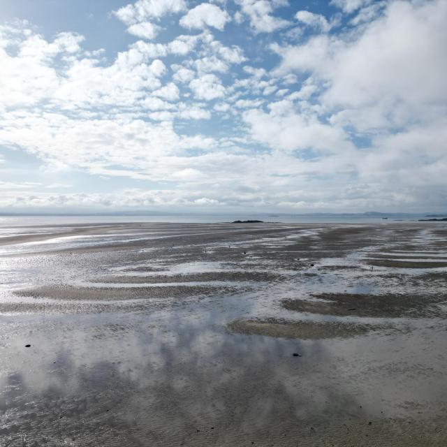 Burntisland beach during low tide. A bright, cloudy sky reflects on shallow pools of water across the sand.