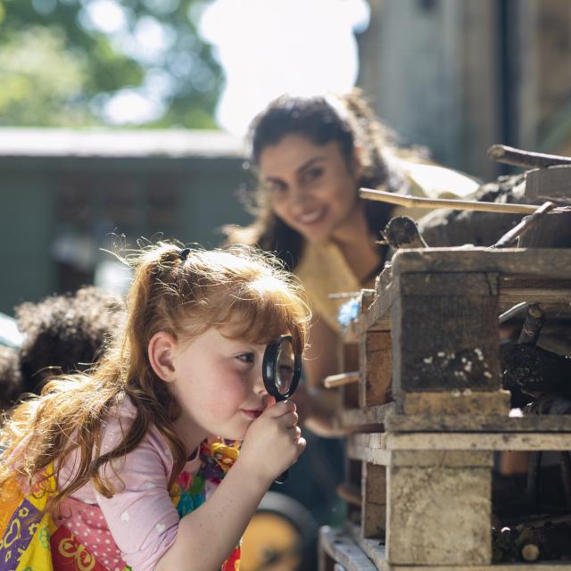 A side view of a girl exploring the bug hotel with a magnifying glass.