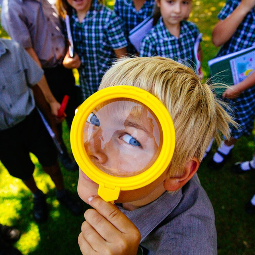 A boy looks through a magnifying glass. Him and his schoolmates have been working with WWF to learn more about nature in their school