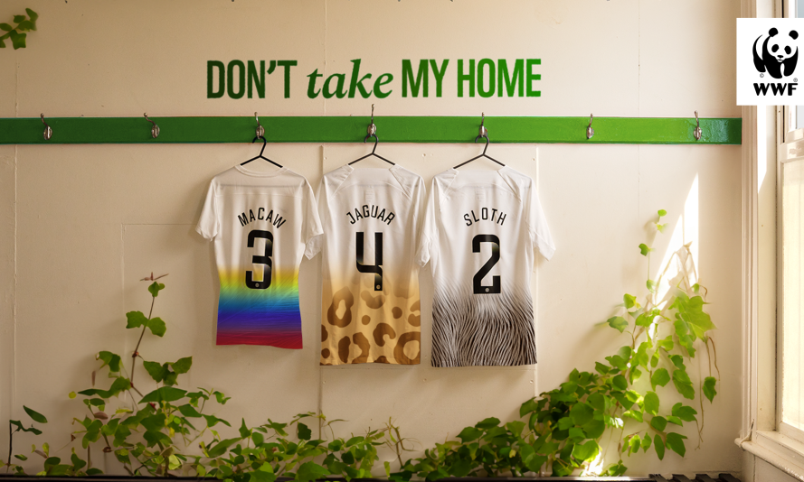 Three football shirts hanging in a changing room below the text reading 'don't take my home'. The shirt names say macaw, jaguar and sloth, representing animals that are impacted by deforestation in the Amazon.