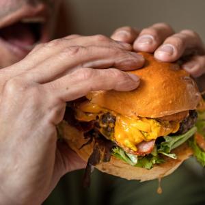 Man about to eat a beef burger with bacon, cheese and lettuce, London, UK. 