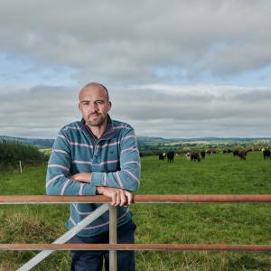 Aled, a farmer in Carmarthenshire, standing behind the gate of his field of cattle.