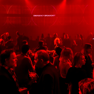 A large room with red stage lighting with people gathered around talking