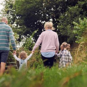The family at Rest Farm, both parents and two children, walk through the field long the hedgerow.