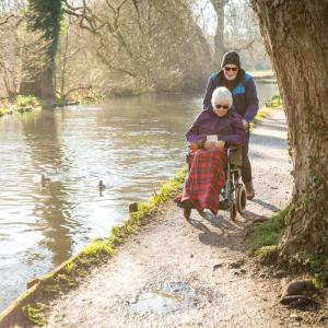 Elderly couple, lady in wheelchair, along riverside in winter