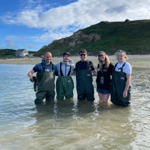 The WWF Cymru team and ambassador Iwan Rheon, knee high in the sea and wearing waders, during a seagrass seed collection trip in Porthdinllaen, Wales