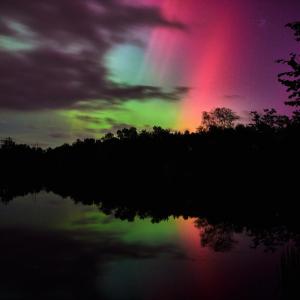 A vibrant aurora borealis display with soft pink, purple, and green lights glowing through a partially cloudy sky