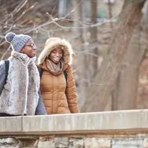 Two women walking over a bridge in nature in the winter
