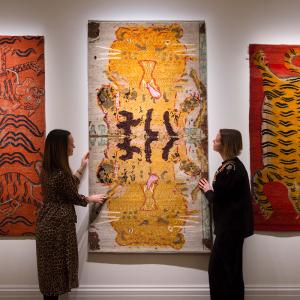 Two women admiring three rug artworks hung on a wall