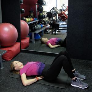 A woman lying on her back in a gym with her hands placed under her back
