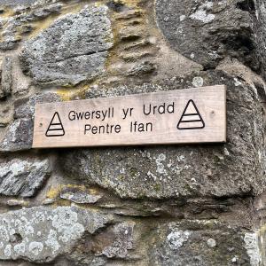 A wooden sign against a stone wall which reads - Gwersyll yr Urdd Pentre Ifan.